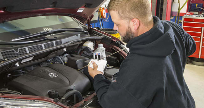 person checking oil of vehicle in body shop